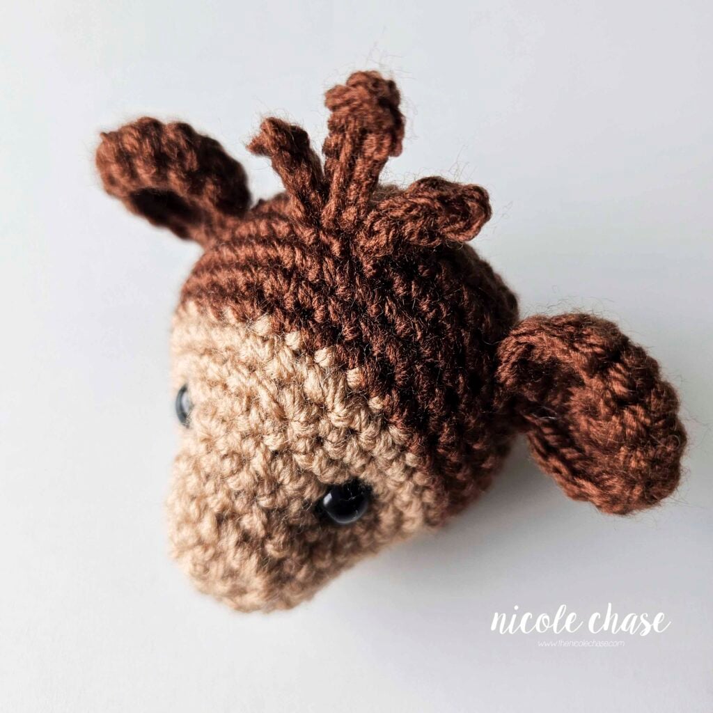 The hair has been sewn into place on the top of the head of the crochet monkey, a side view. 