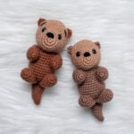 Two finished crochet sea otters, Ollie the Otter, showing the front and side view of the amigurumi project on a white fluffy surface.