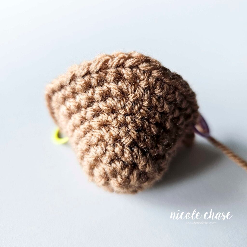 The head of the crochet otter after the completion of R8, shown in a light brown yarn. Two stitch markers are visible on each side of the head.