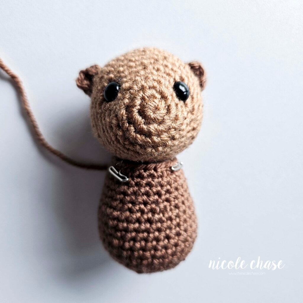 The body has been pinned into place on the bottom of the otter's crochet head with the nose of the head facing straight out and the pieces are ready to be sewn.