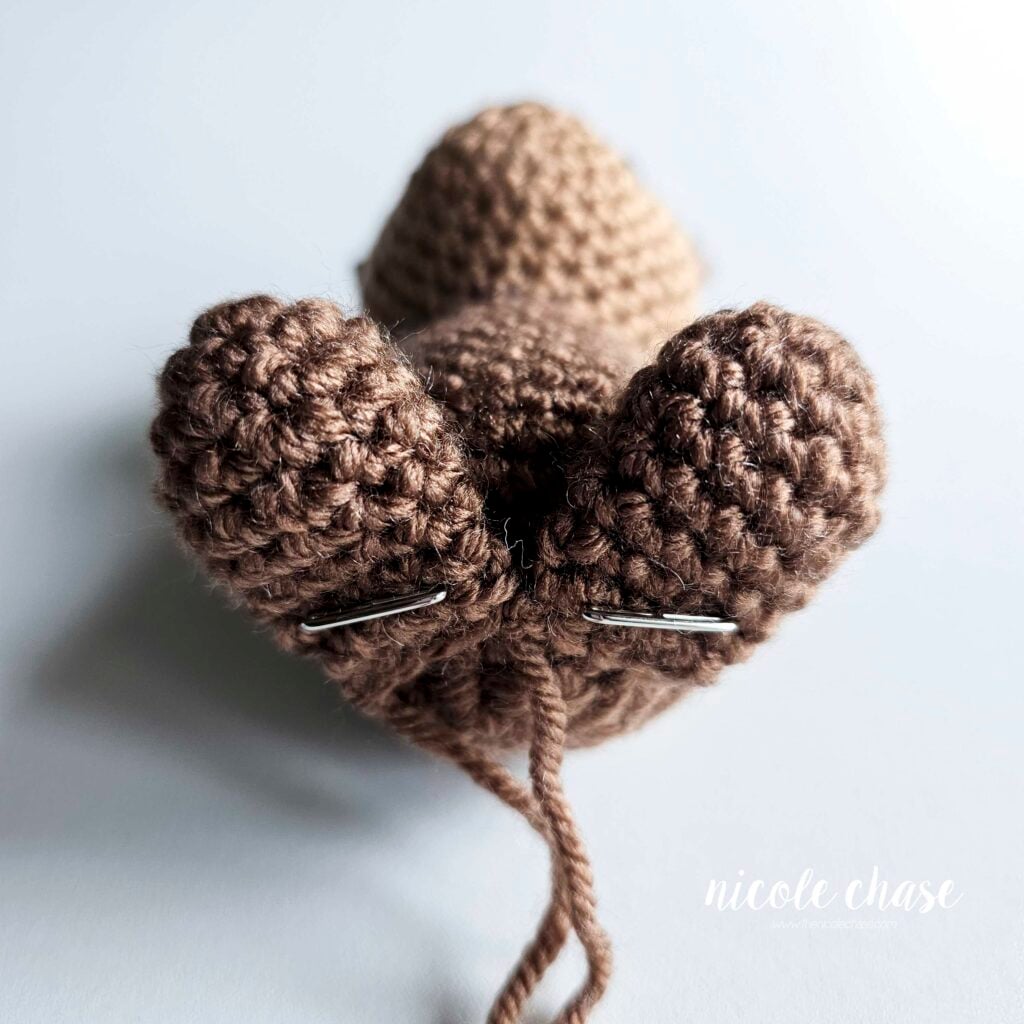 The two legs of the crochet otter have been pinned into place on the front of the body and are ready to be sewn.