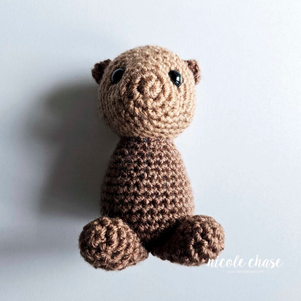A front view of the two crochet legs of the otter sewn into place on the bottom front of the body.