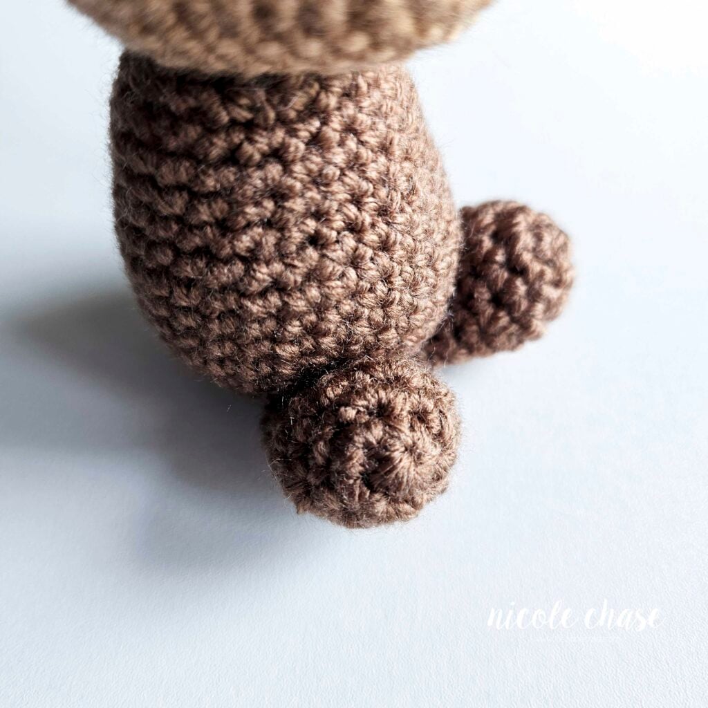 A side view of the crochet legs of the otter sewn into place on the front of the body.