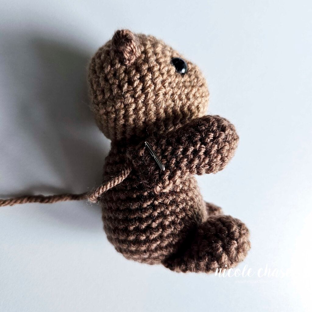 The arms of the crochet otter are pinned into place on the side of the body and are ready for sewing.