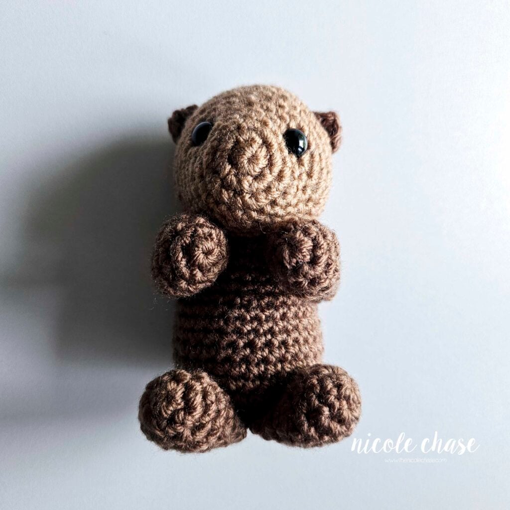 The crochet otter's arms are sewn into place and are brought together in the front of the body.