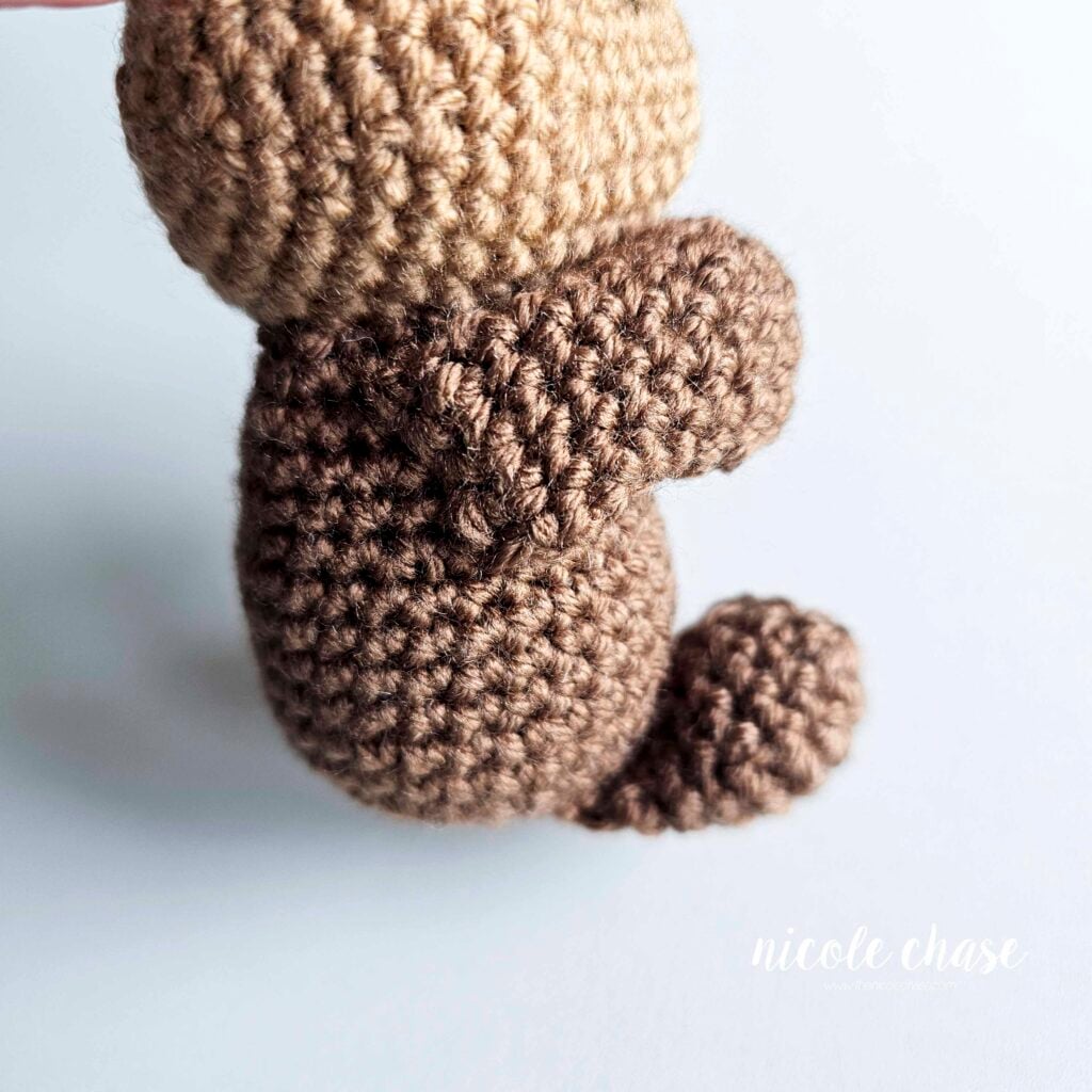 A side view of the otter's arms sewn into place on the side of the crochet body.