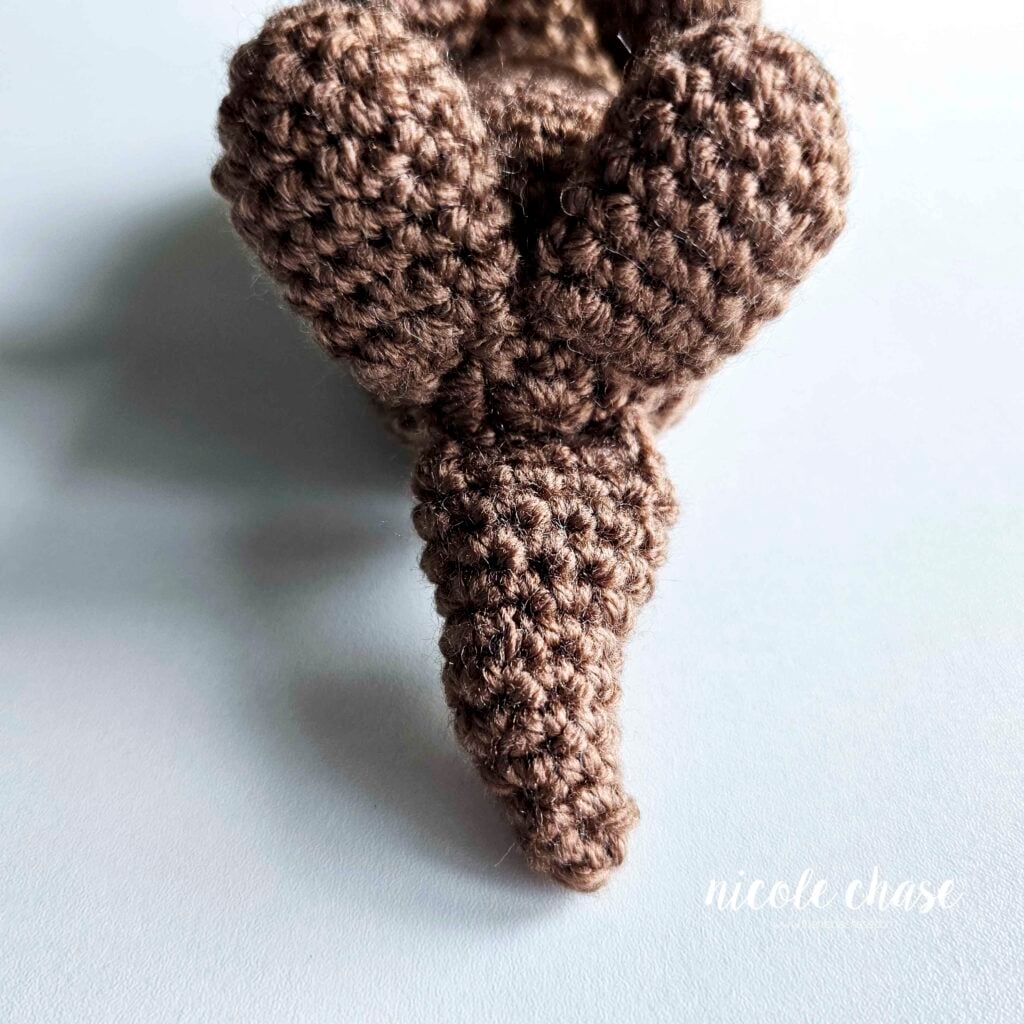 A front view from the bottom of the crochet otter's body, demonstrating the amigurumi tail sewn into place.