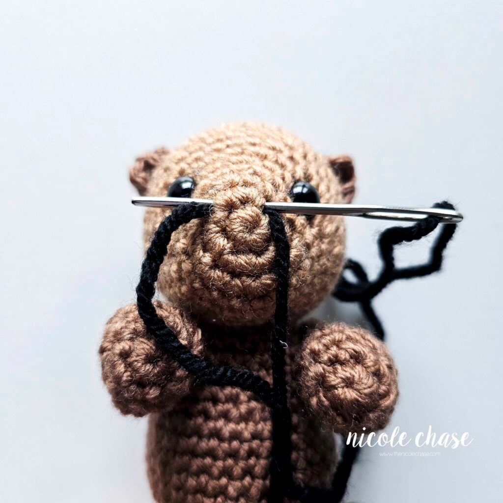 The black yarn has been looped around to start creating the nose of the amigurumi otter.
