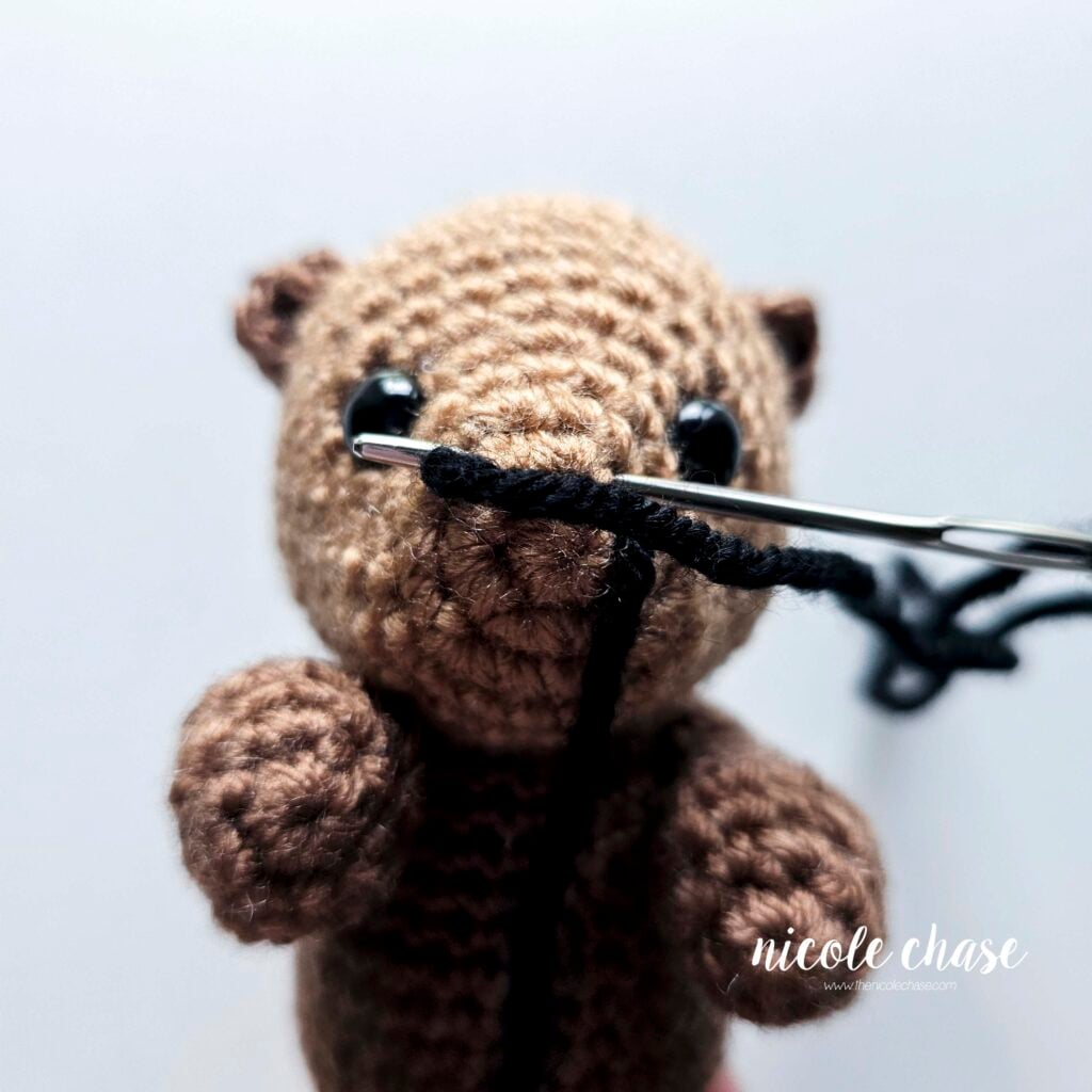 Embroidering the otter's nose with black yarn by continually looping the black yarn around the front of the face.