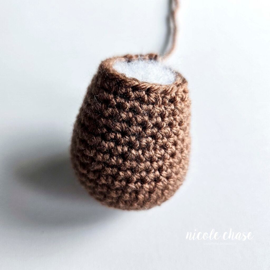 The finished body of the crochet otter shown in brown yarn and filled with stuffing, ready for assembling.