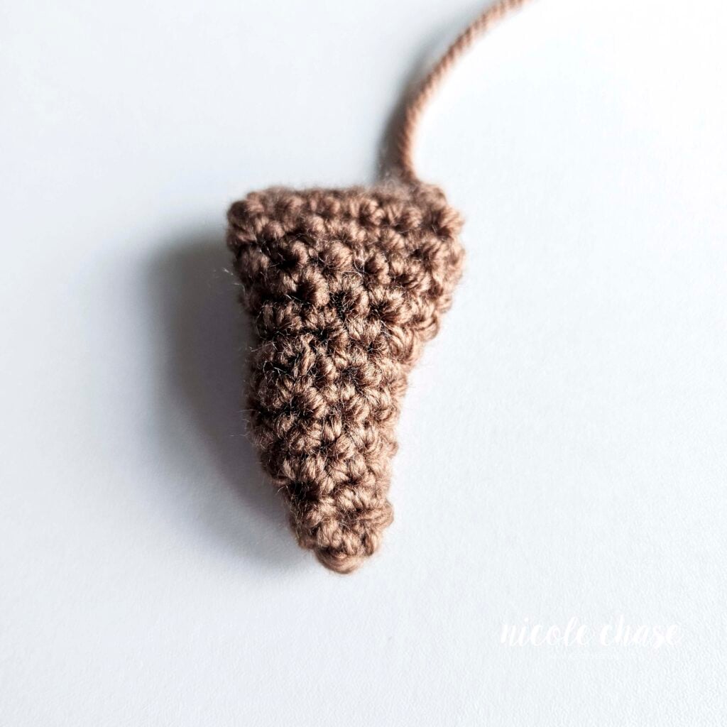 The brown crochet tail of the otter, filled with stuffing. The tail curves to one side. This piece is ready for assembling.