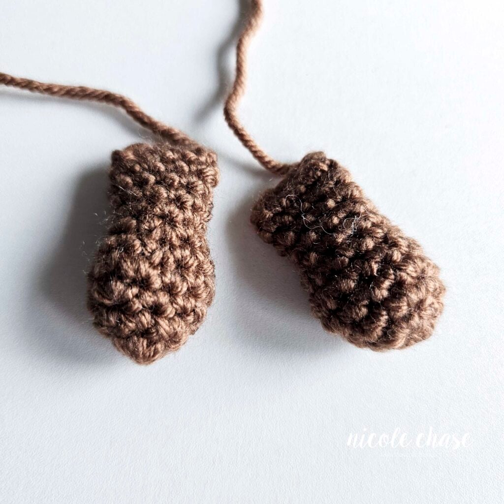 Two crochet arms for the amigurumi otter named Ollie, both are made in a brown yarn and are filled with stuffing and awaiting assembly.
