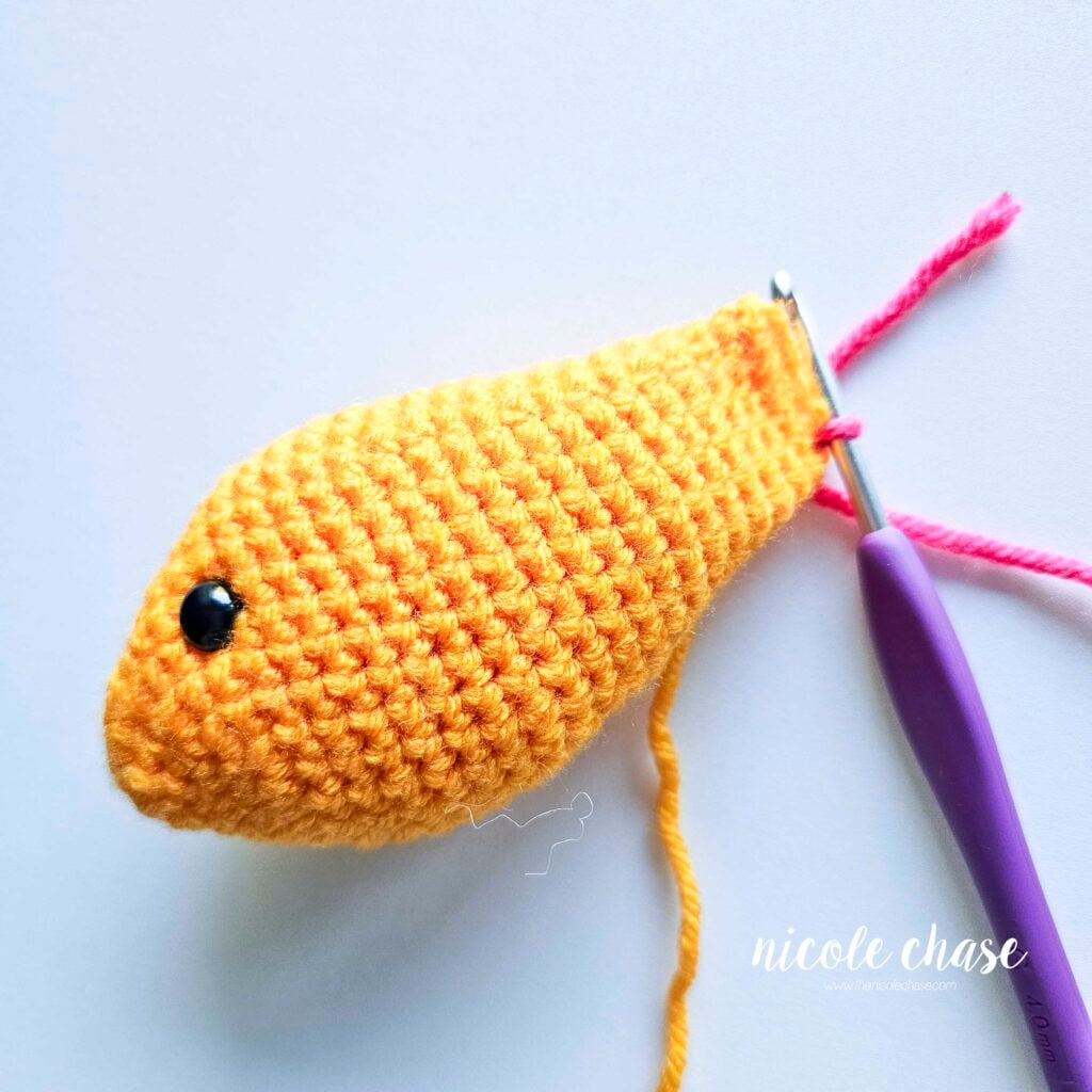 Attaching the pink yarn to the last round of the fish body to start the tail fin.