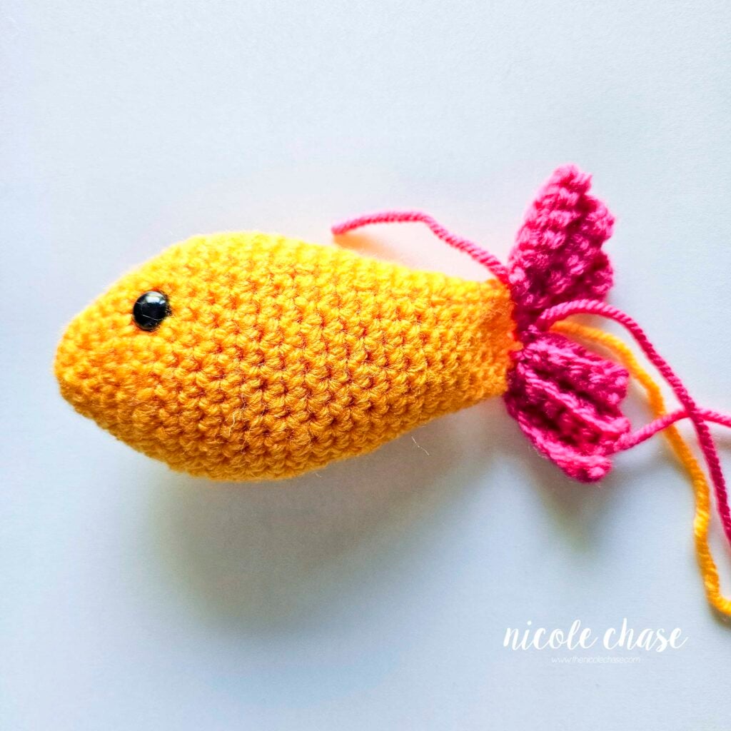 The tail fins of the crochet fish have been completed and the yarn tails are ready to be hidden inside the piece.