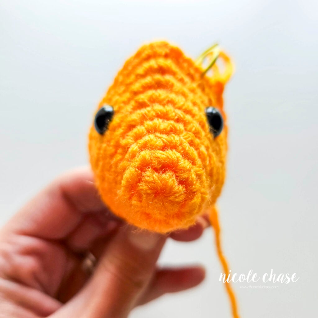 The face of the crochet fish after R9 to demonstrate the placement of the black safety eyes, a front on view.