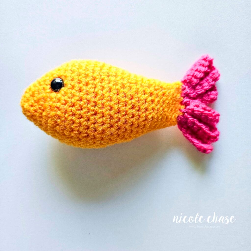 The yarn tails of the crochet fish's tail fin have been hidden inside the piece and they are complete.