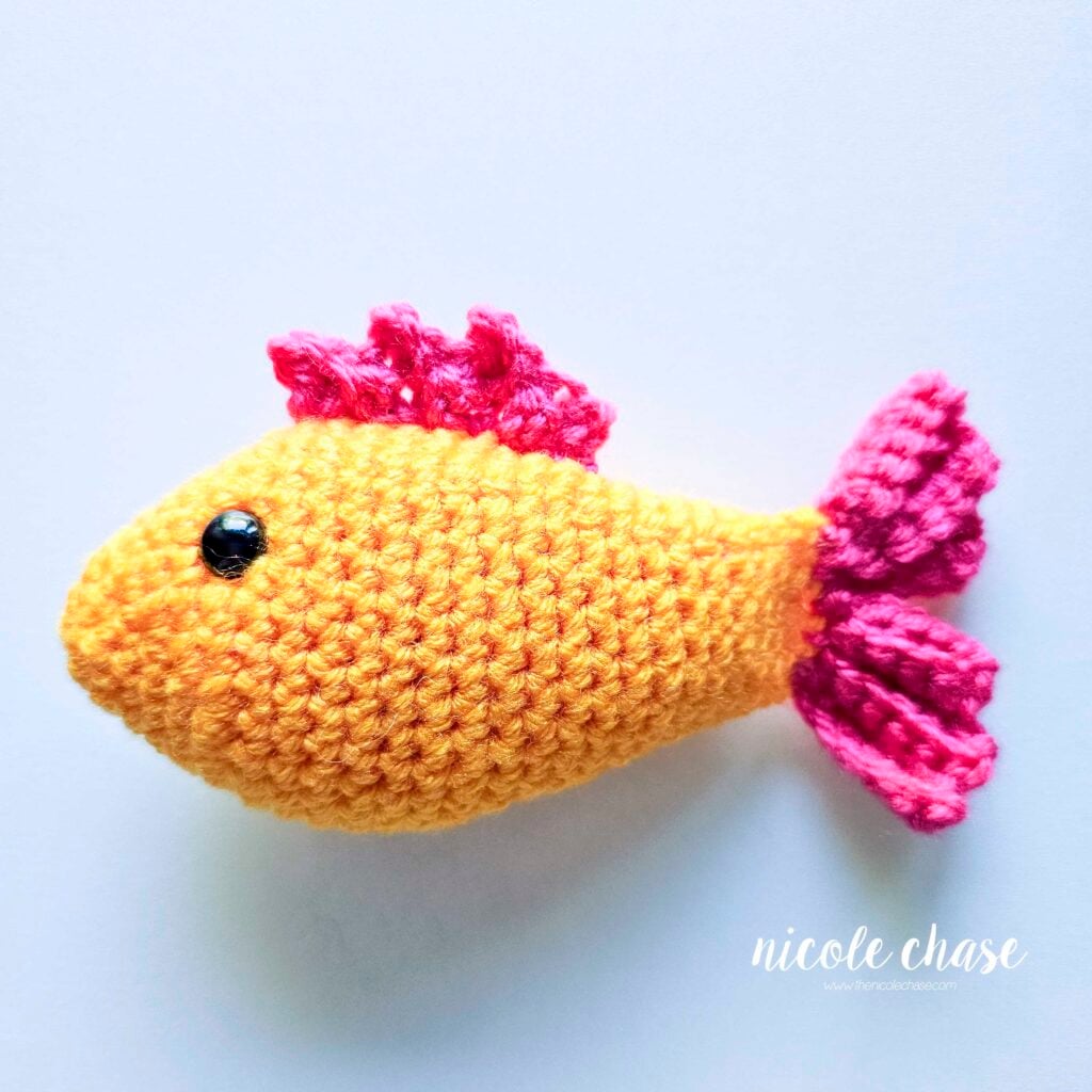 A side view of the top fin being sewn onto the top of the crochet fish.