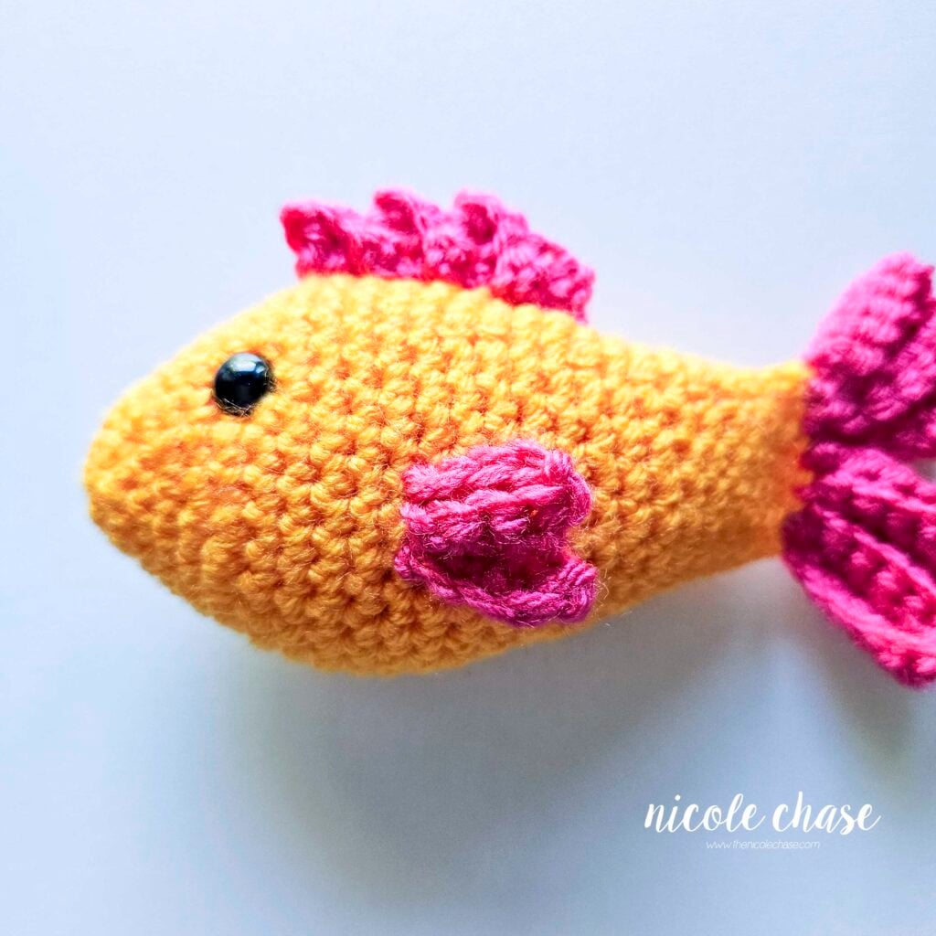 The side fin has been sewn into place on the side of the crochet fish body.