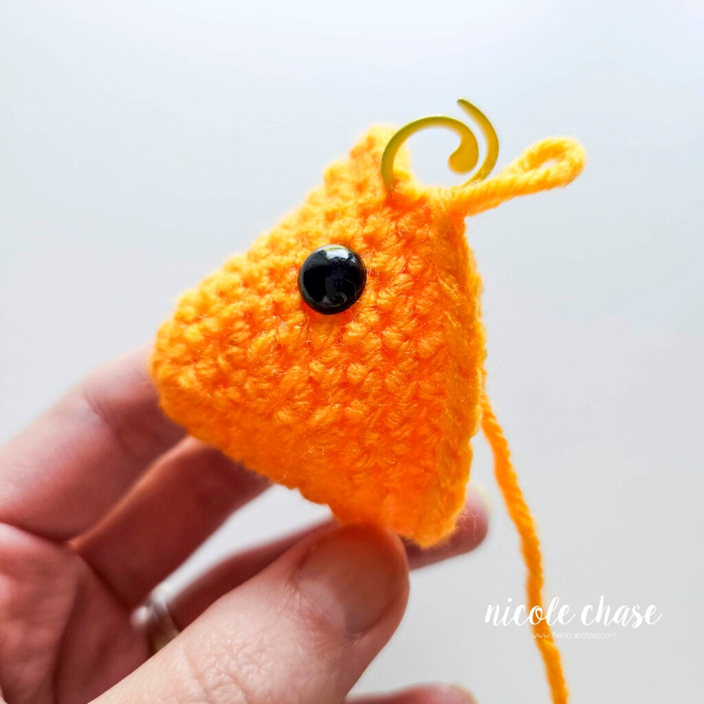 The face of the crochet fish after R9 to demonstrate the placement of the black safety eyes, a side view.