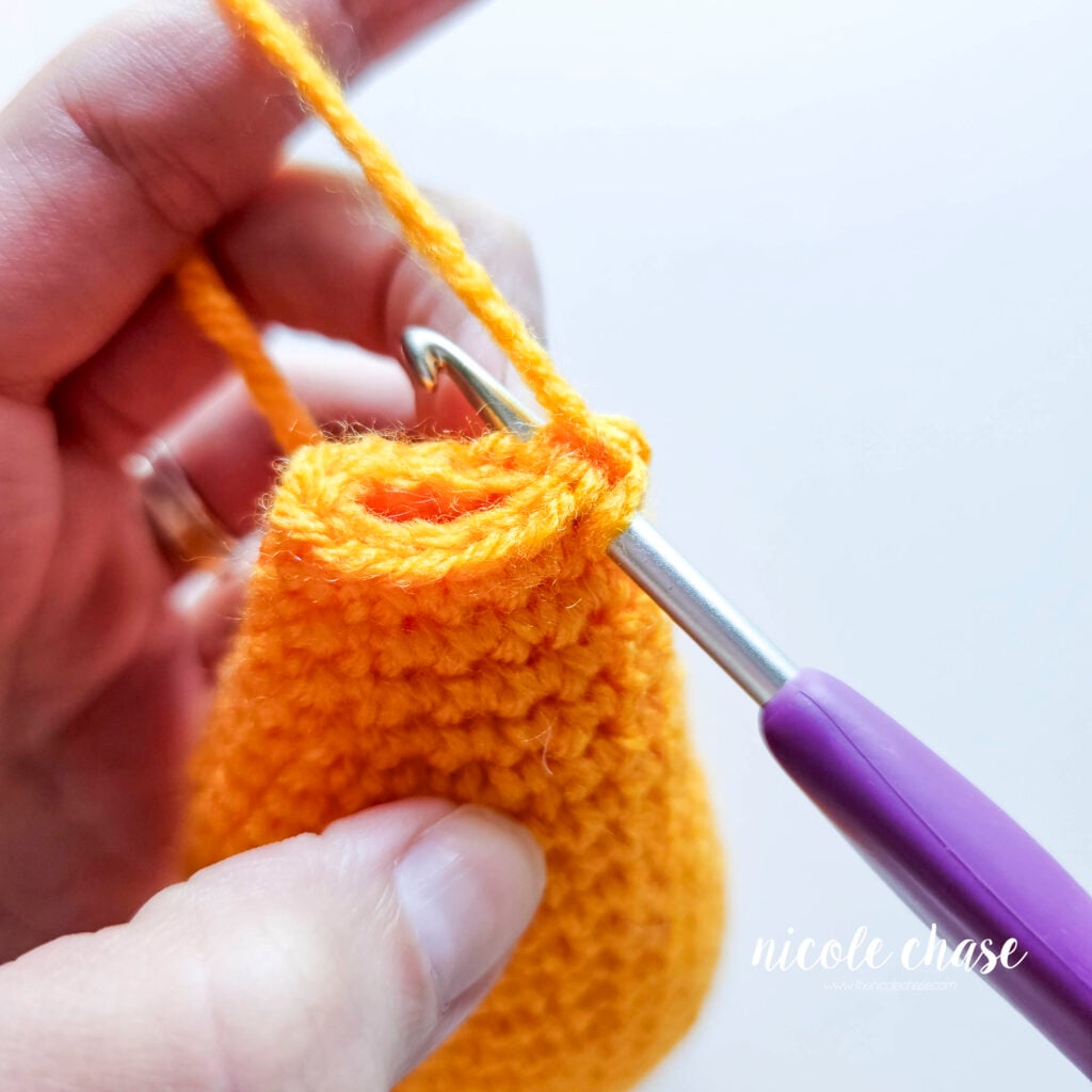 The end of the fish is folded closed and are being crocheted together. A hook is inserted across the two sides.