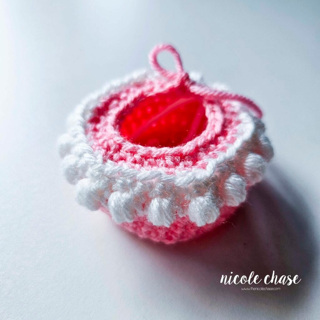 The first tier of the crochet birthday cake has been completed in pink yarn with white puffy stitches for the frosting.