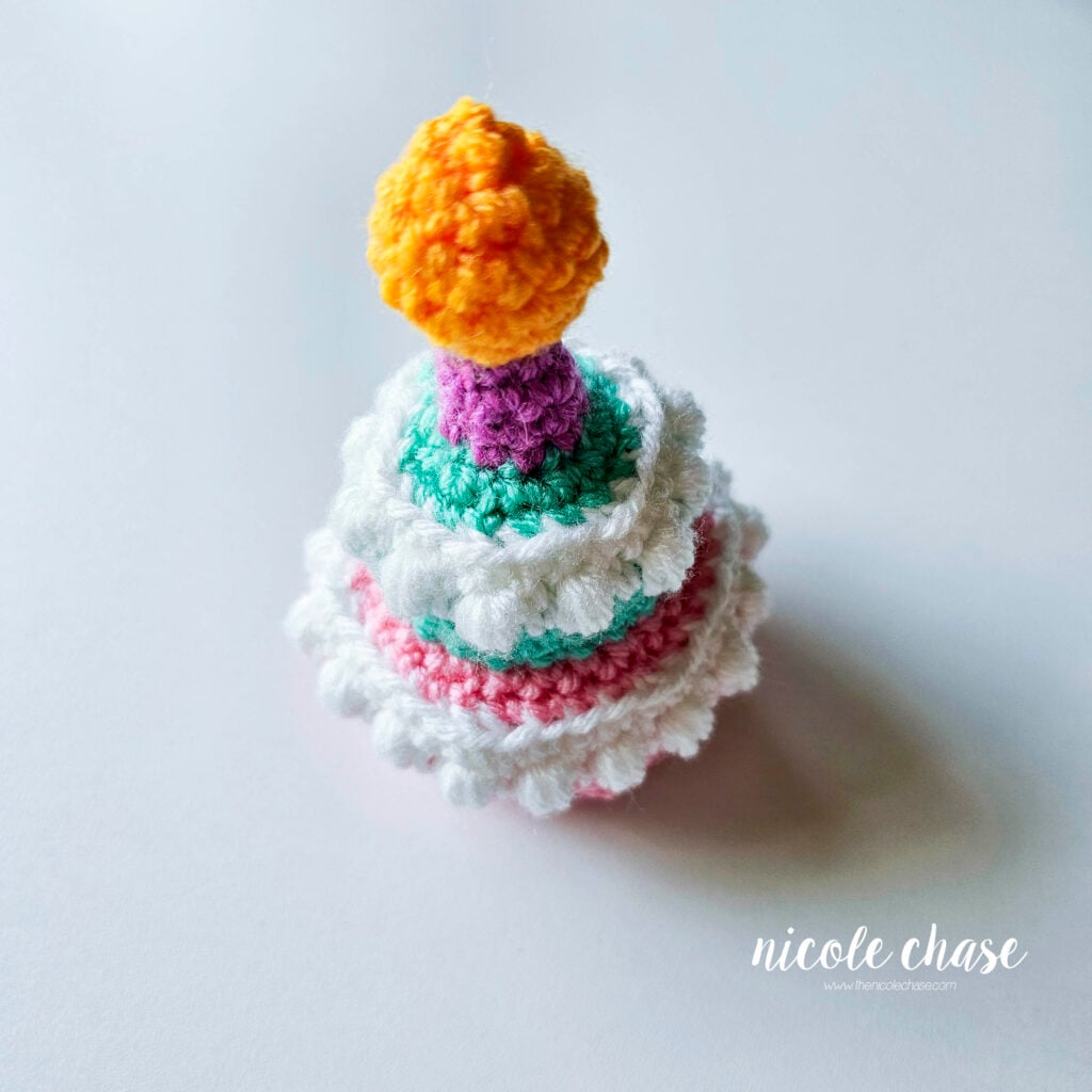 The candle and flame have been crocheted on the crochet birthday cake pattern in purple yarn with a yellow flame.