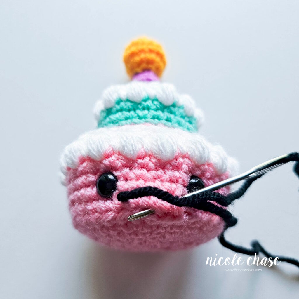 The black yarn has been looped around the starting stitches and the yarn needle is pushed to the area where the dip in the smile will be.