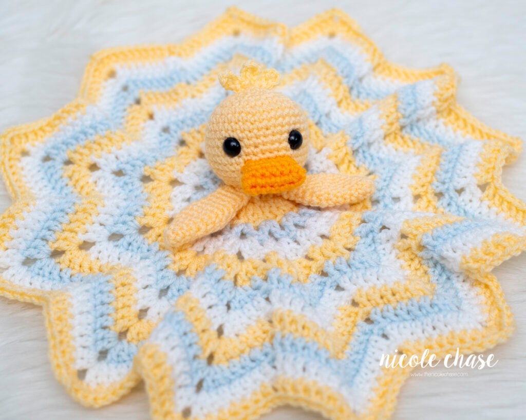 Finished Hug Me Duck Lovey featuring a pastel yellow crochet duck head with an orange beak attached to a star-shaped striped baby blanket.