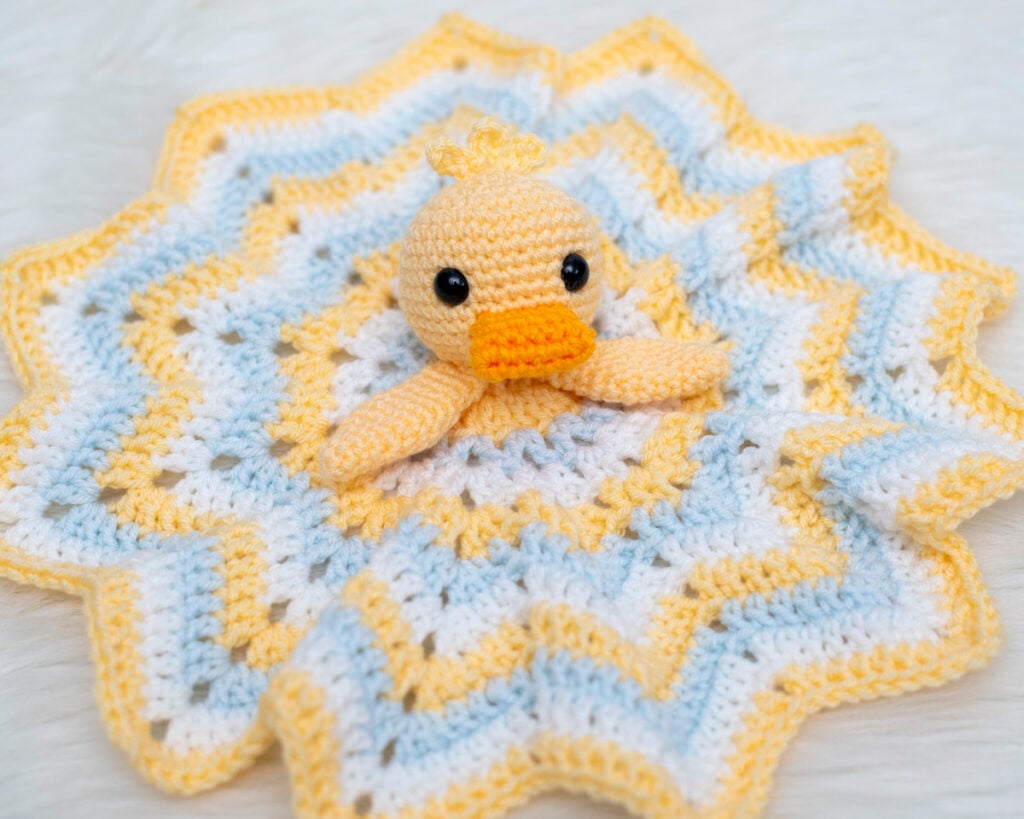 Crochet duck lovey security blanket with a yellow duckling amigurumi head on a star-shaped yellow, light blue, and white blanket.