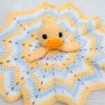 Crochet duck lovey security blanket with a yellow duckling amigurumi head on a star-shaped yellow, light blue, and white blanket.