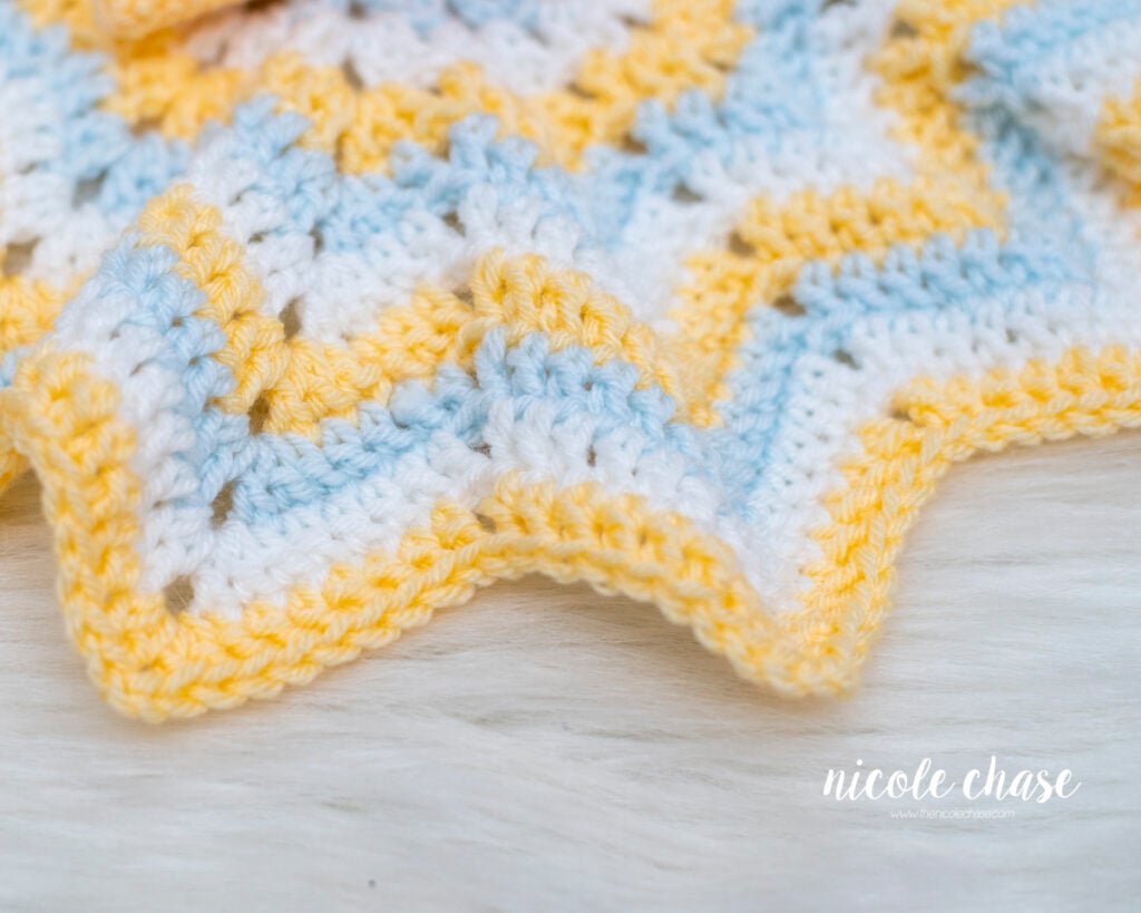 Close-up view of the star-shaped crochet lovey blanket edge, showing the ripple pattern stitches in yellow, white, and light blue yarn.
