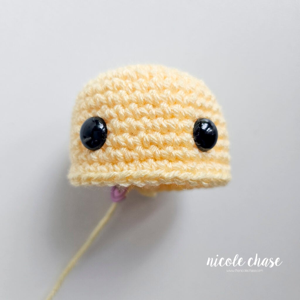 Yellow crocheted duck head work-in-progress showing safety eyes inserted to demonstrate the proper placement,