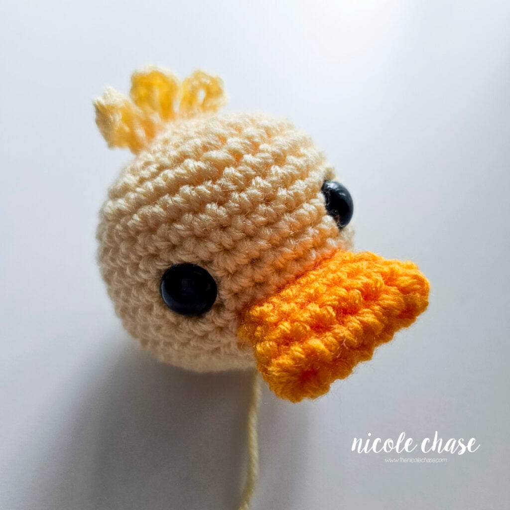 Side profile view showing the completed duck head with attached tuft and orange bill.