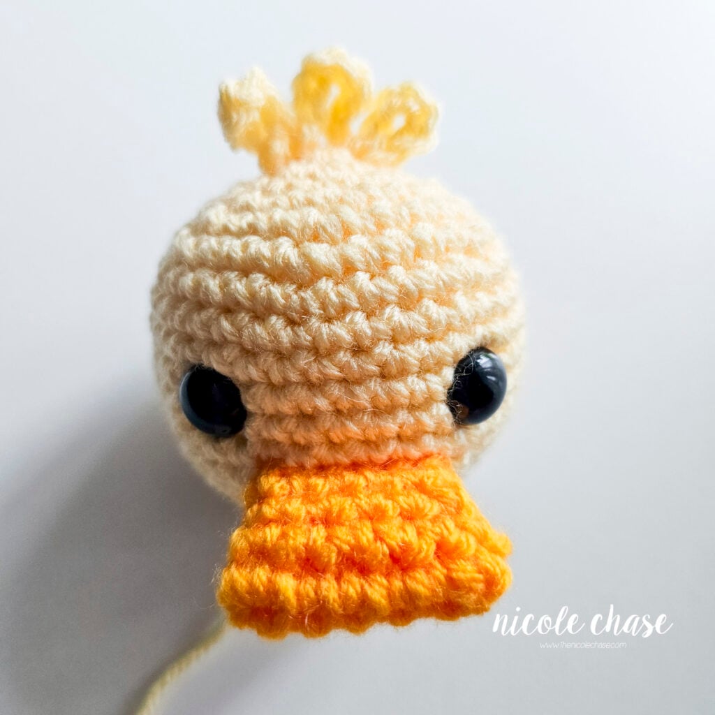 Front, top down view of the crochet orange bill sewn into place on the head of the crochet duck.