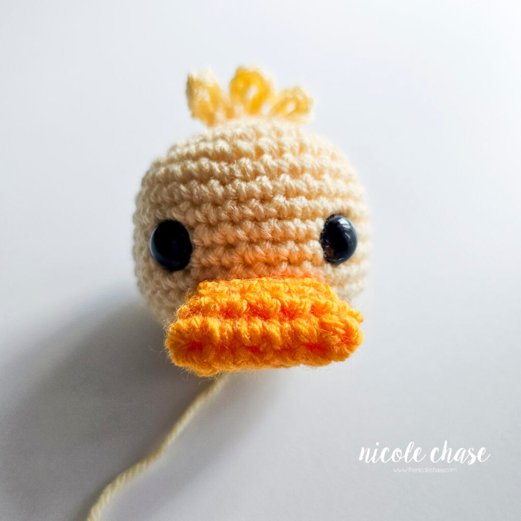 Front view of the yellow crocheted duck head with the orange bill fully sewn in place below the eyes.