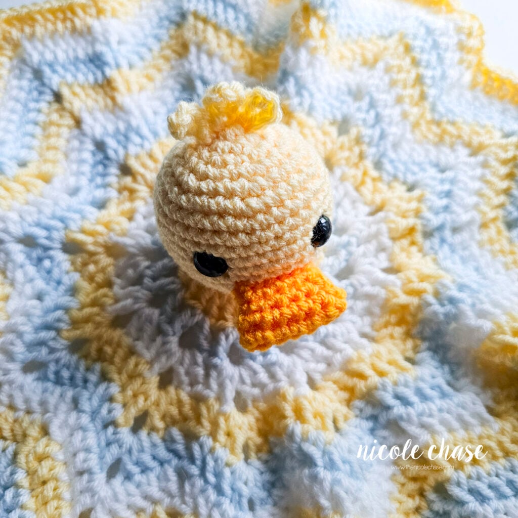 Top-down angle showing the duck head securely stitched to the center of the star-shaped crochet blanket.