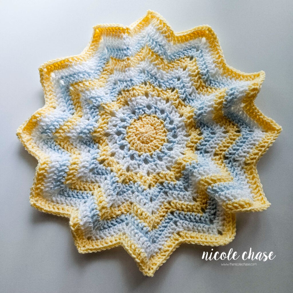 Completed star-shaped crochet lovey blanket with alternating yellow, light blue, and white ripple stripes.