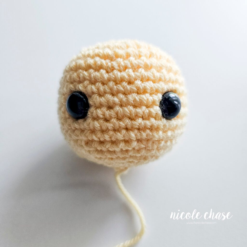 Completed light yellow crocheted duck head fully stuffed with black safety eyes set in place.