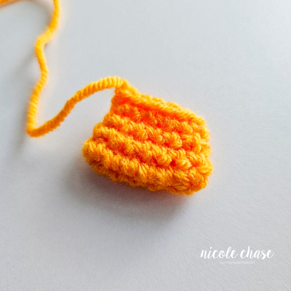 Completed bright orange crocheted duck bill piece with a yarn tail attached for sewing.