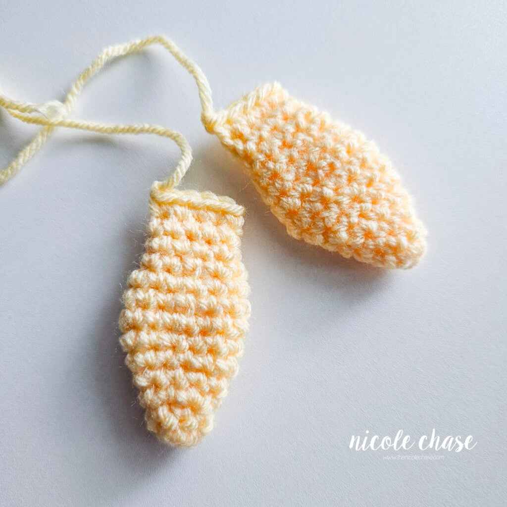 Pair of completed pale yellow crocheted duck wings lay flat with long yarn tails left for attachment.