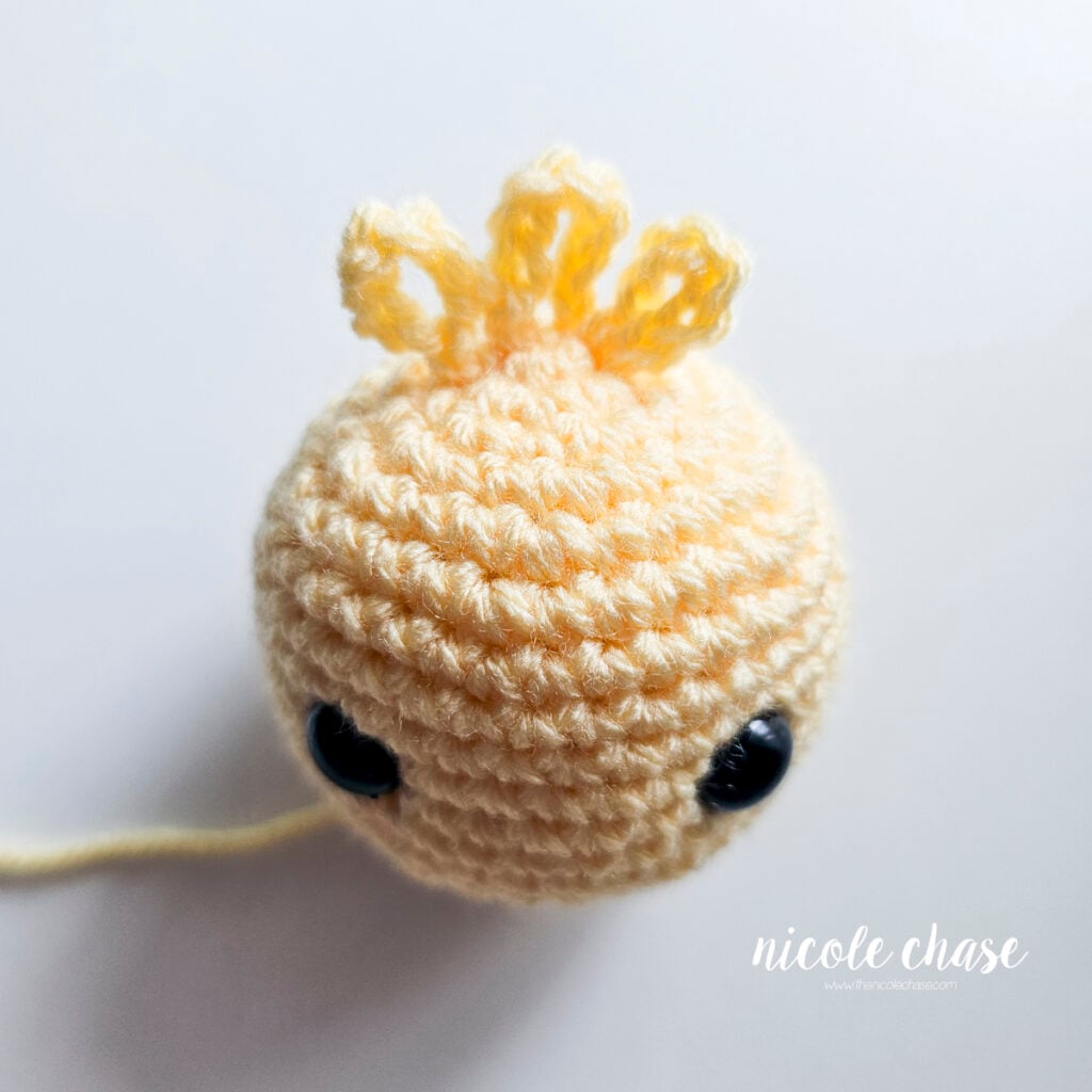 Top-down view showing the crocheted feather tuft attached securely to the top of the yellow duck head.
