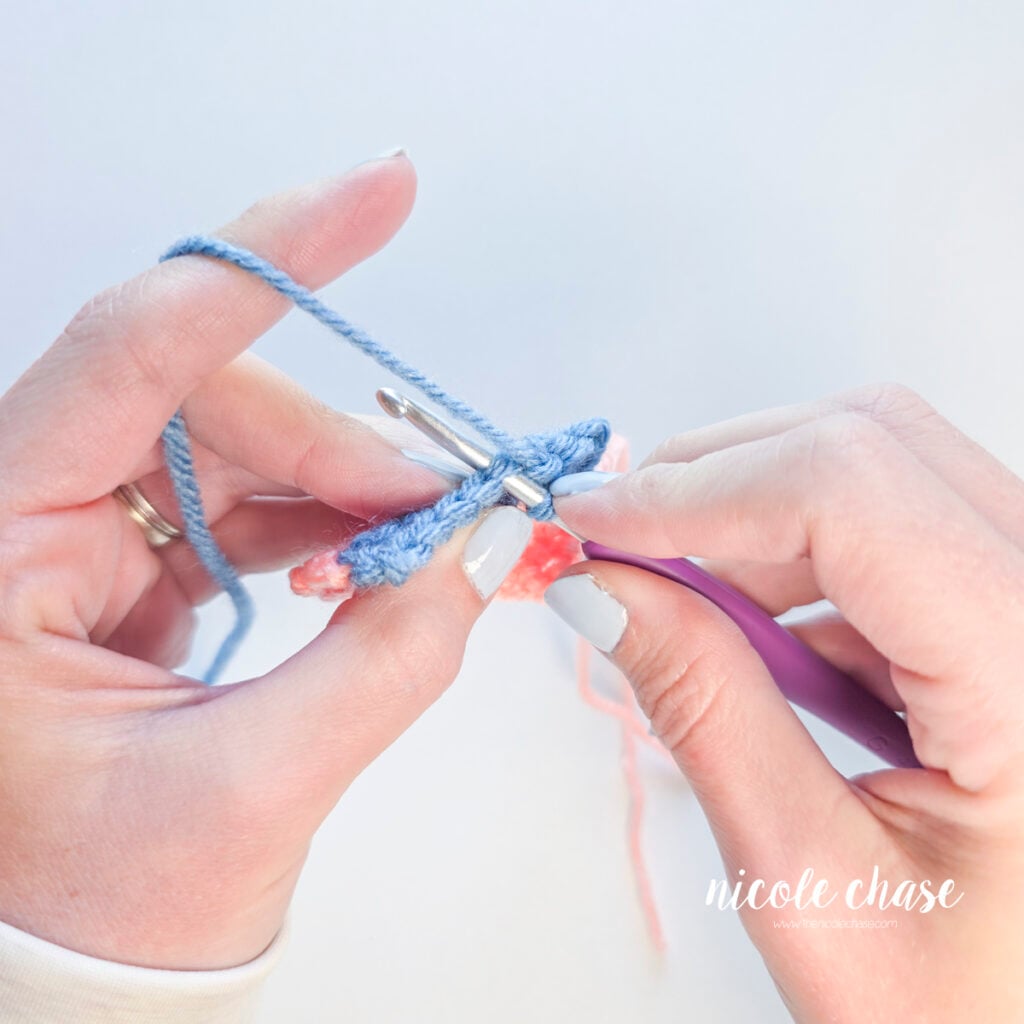 Inserting a crochet hook under the top loops of a blue single crochet stitch.