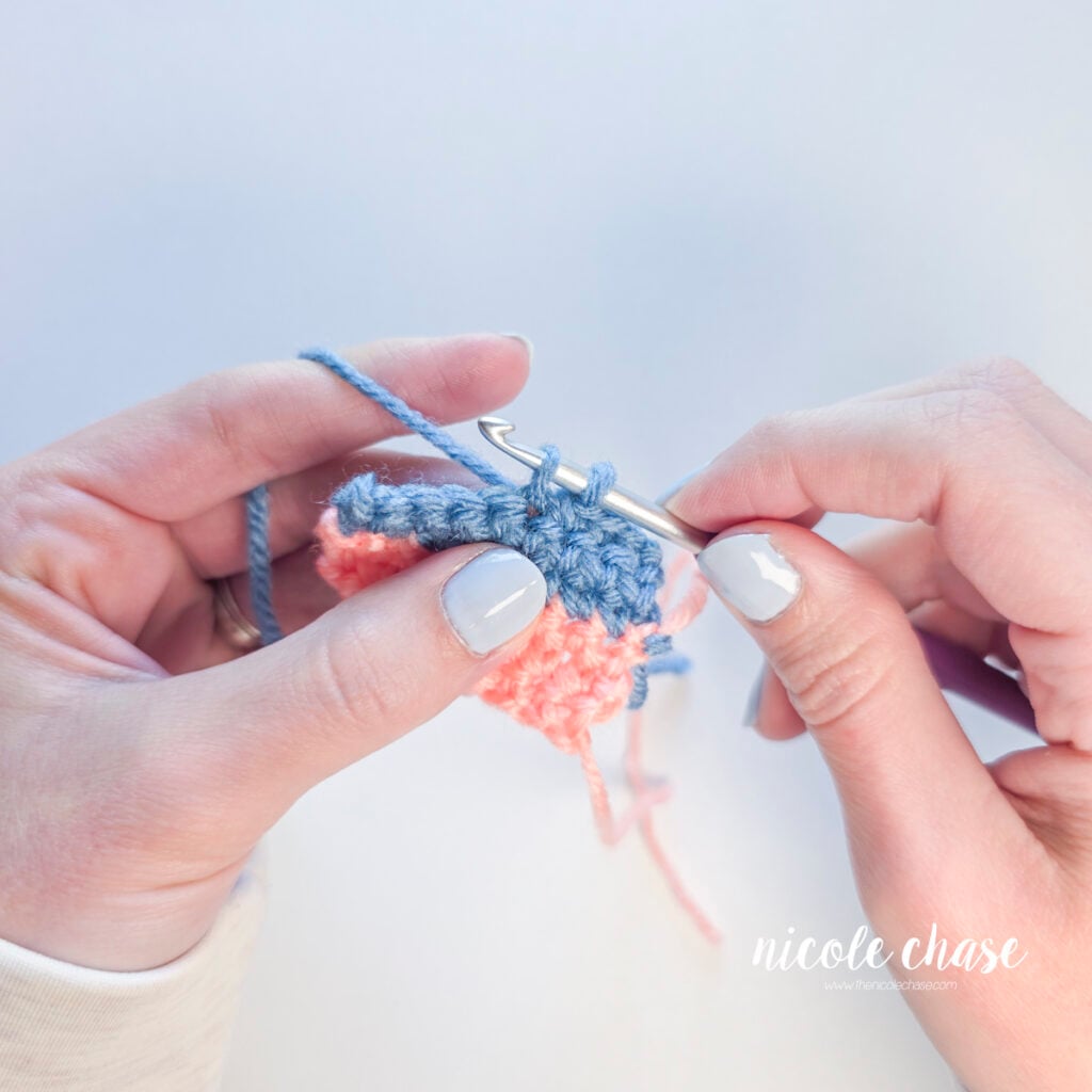Two blue yarn loops resting on a purple crochet hook before completing the stitch.