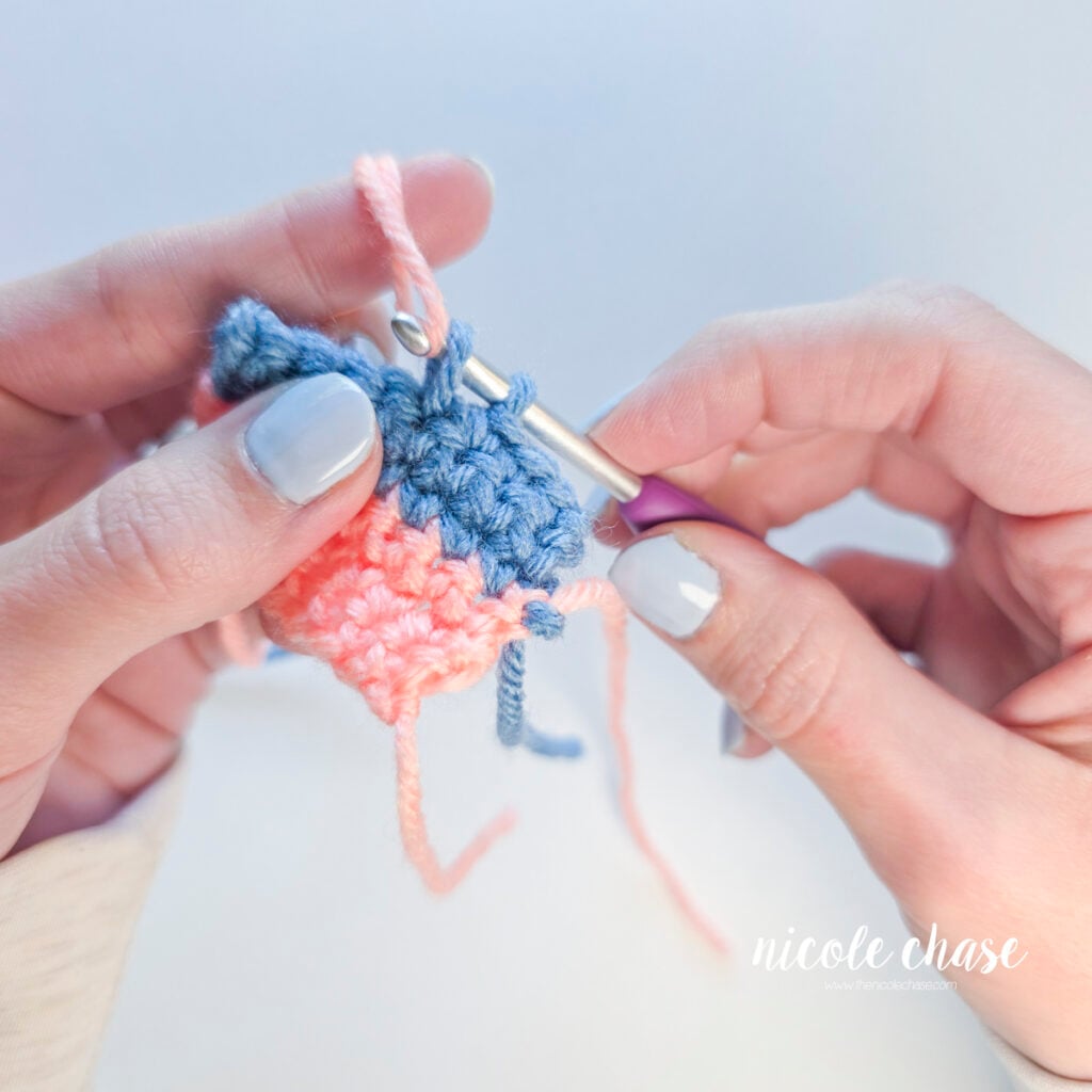 Pulling pink yarn through two blue loops on a crochet hook to finish the single crochet stitch.