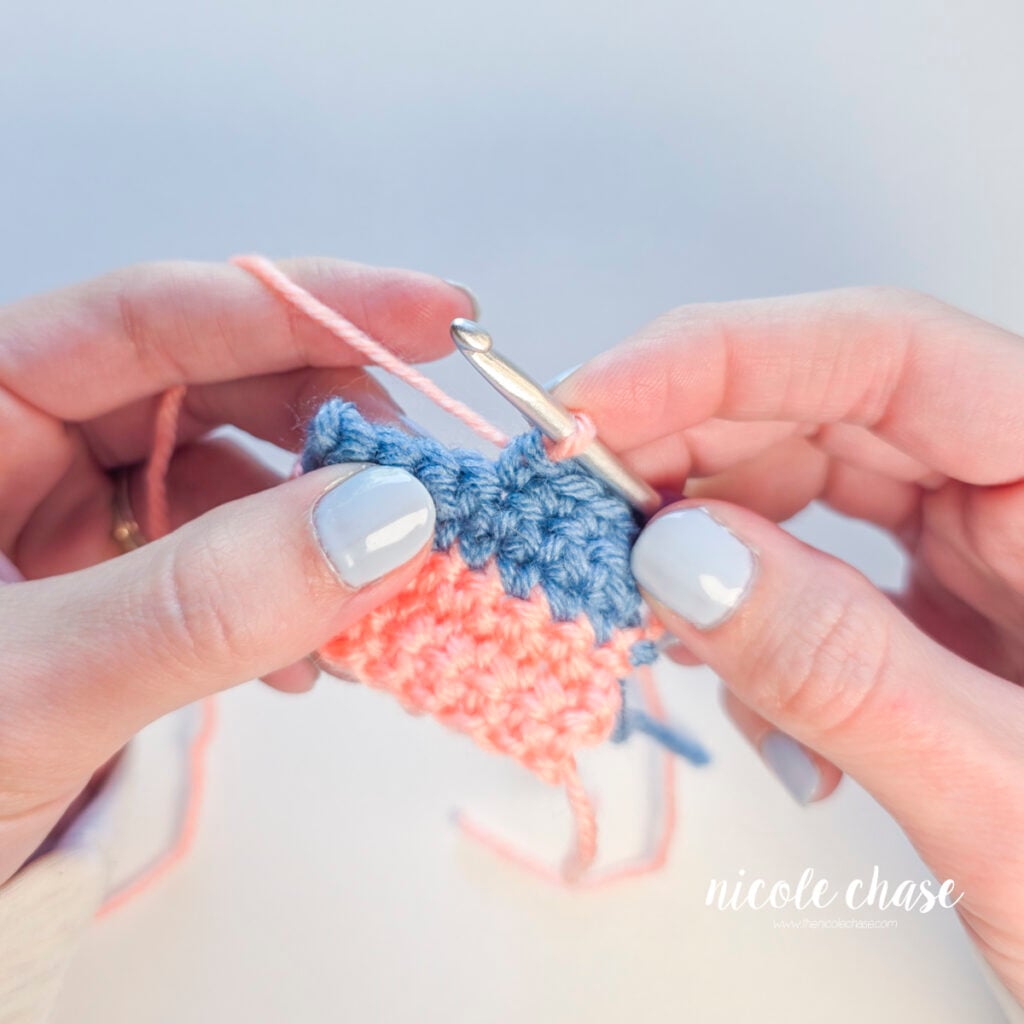 The yarn tails have been secured and the loop of pink yarn is shown on the hook, ready to begin the next stitch.