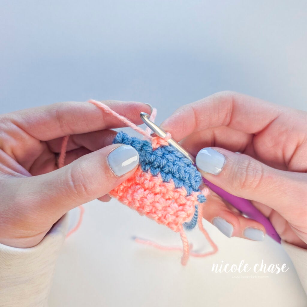 The first single crochet stitch in pink yarn has been made across the blue row.