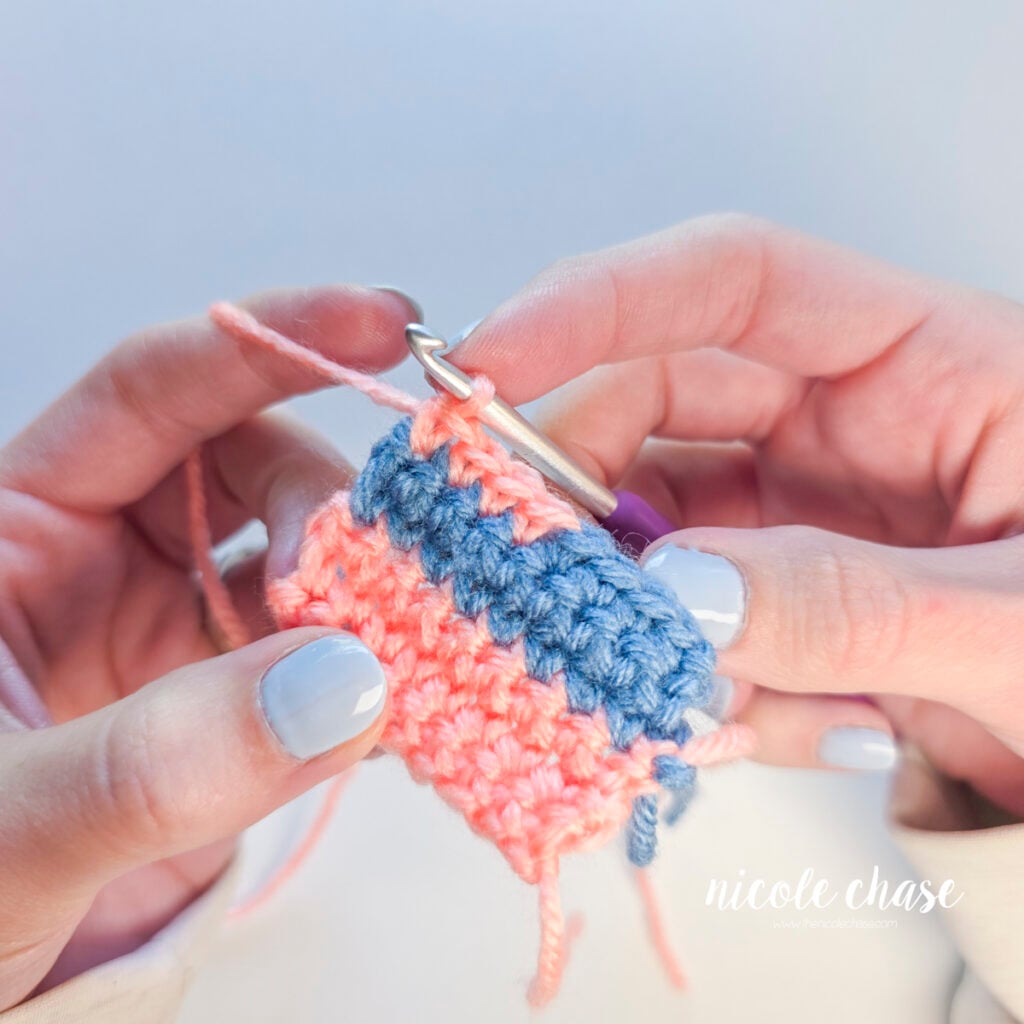 The row has been completed with pink single crochet stitches on a blue and pink swatch.