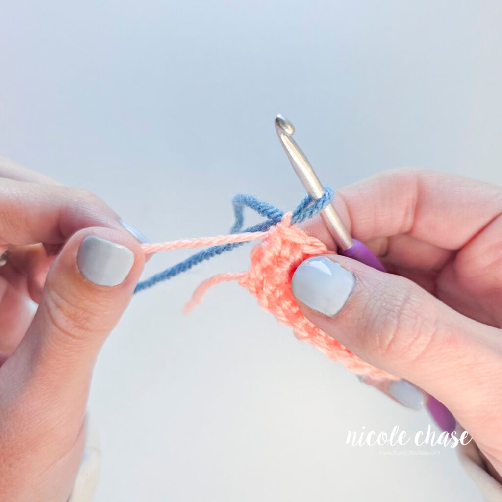 Hands pulling the pink yarn tail down to shrink the pink loop of yarn.