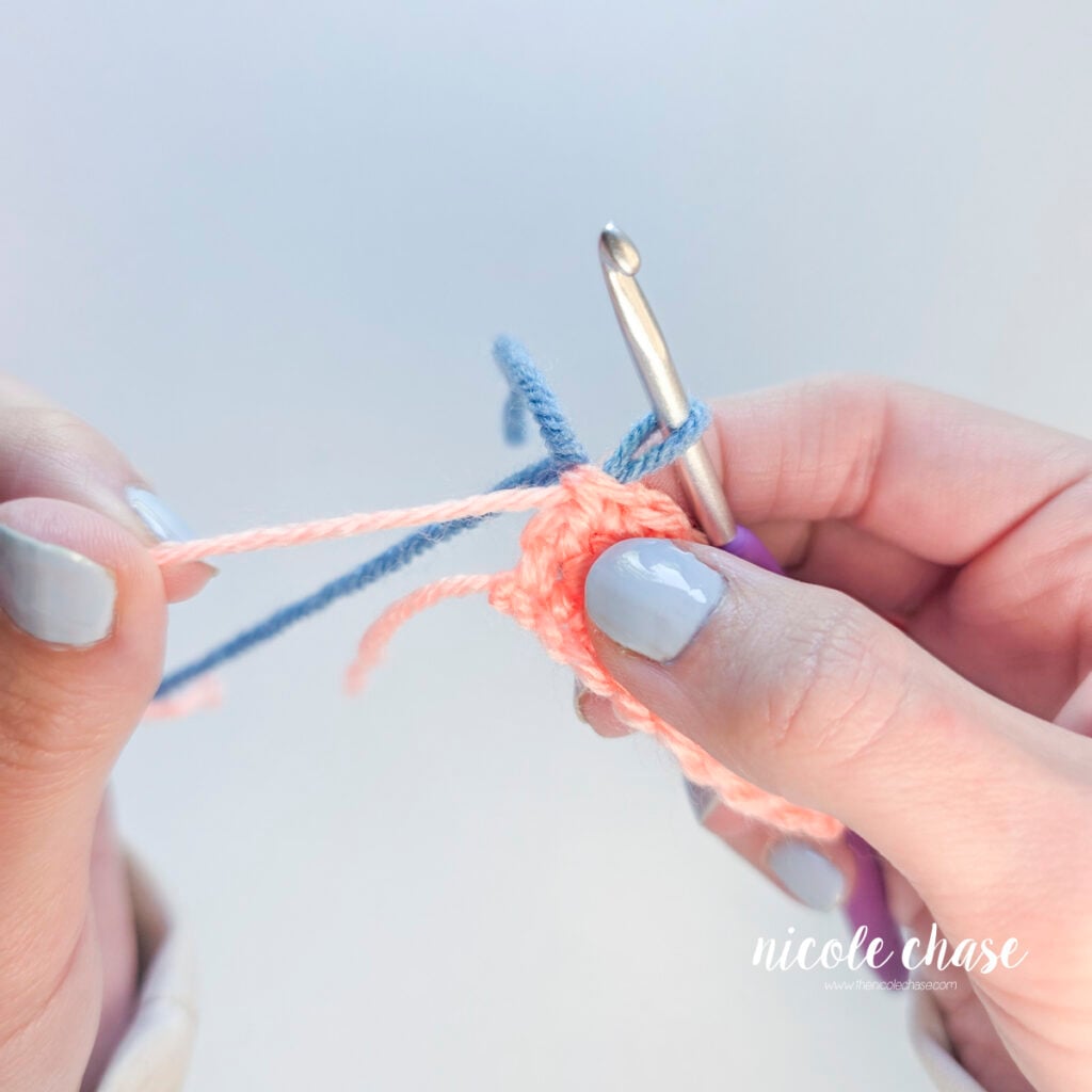 Close up of the pink yarn tail being pulled tight so only a blue loop remains on the crochet hook.