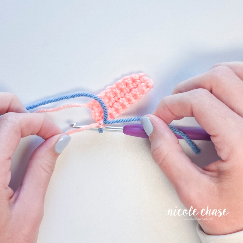 Hands tying yarn tails underneath the crochet hook to secure the color change.